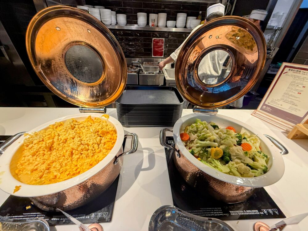 桃園国際空港ラウンジのビュッフェに並ぶスクランブルエッグと温野菜の温かい料理
