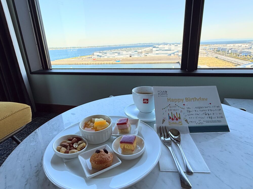 フォーポイントバイシェラトン名古屋中部国際空港からの誕生日サプライズ。Happy Birthdayのメッセージカードとミニケーキ・フルーツゼリー・ナッツ・マフィンのスイーツプレート、illyコーヒーが提供されている。