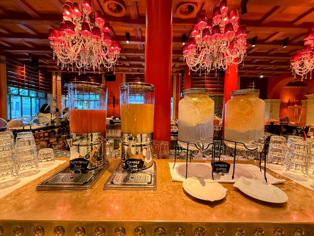 マルチビタミンジュース、オレンジジュース、レモン入りインフューズドウォーターのディスペンサーが並ぶドリンクコーナー。
