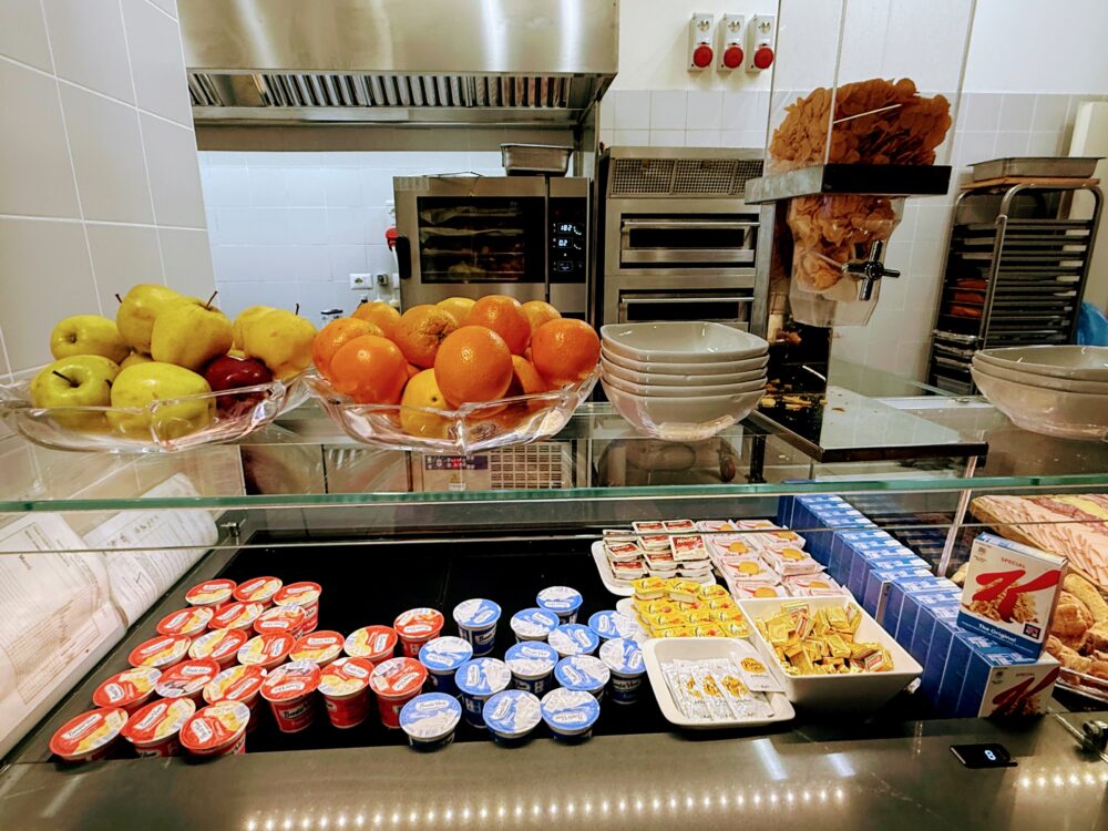 Prima Vista Loungeのビュッフェ。リンゴやオレンジなどのフルーツ、ヨーグルト、クラッカーが並ぶ軽食コーナー。