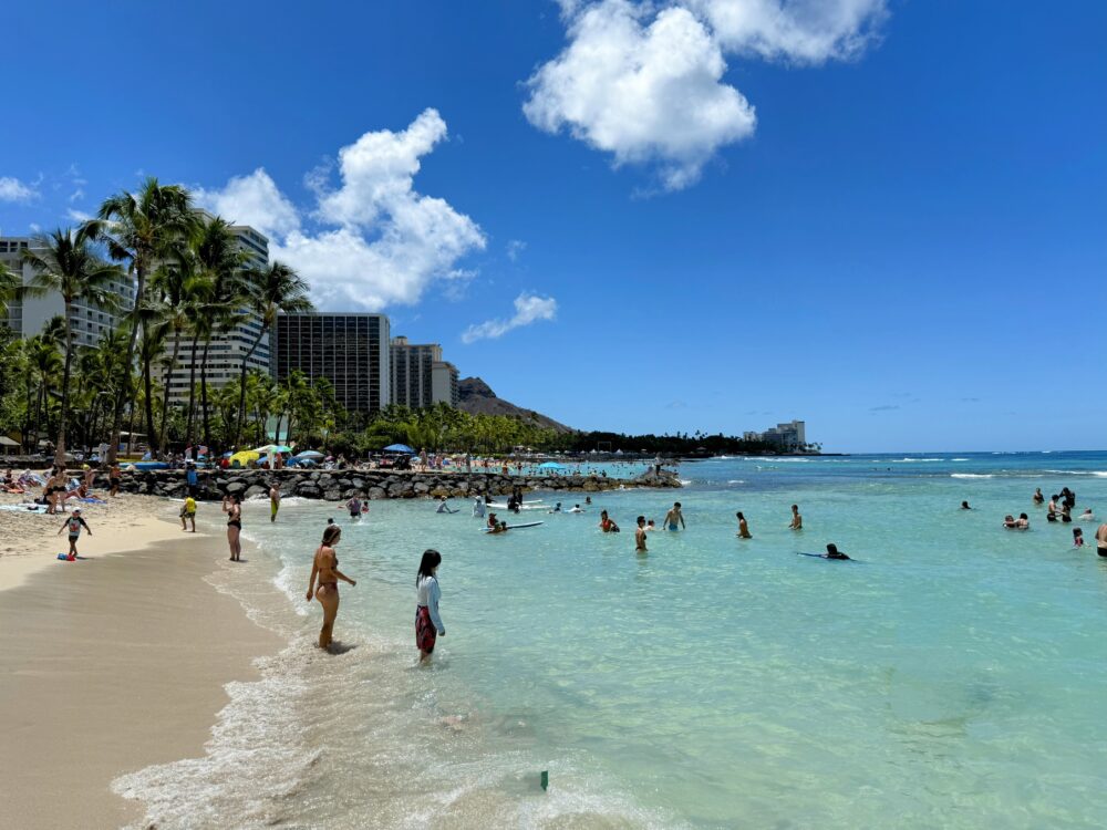 ワイキキビーチの美しい風景。多くの人々が海や砂浜で楽しんでおり、遠景にダイヤモンドヘッドが見える。