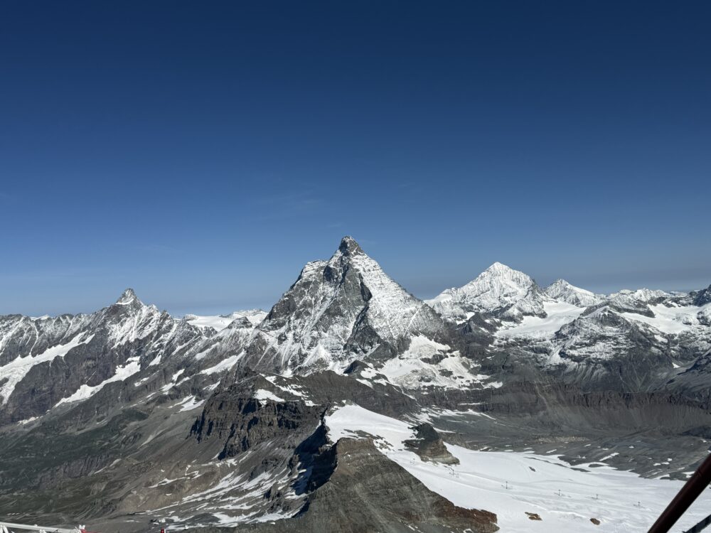 マッターホルン・グレッシャーパラダイスから見下ろす広大な雪原と氷河。遠くには連なる山々がそびえ、空は一点の雲もない真っ青な色をしている。
