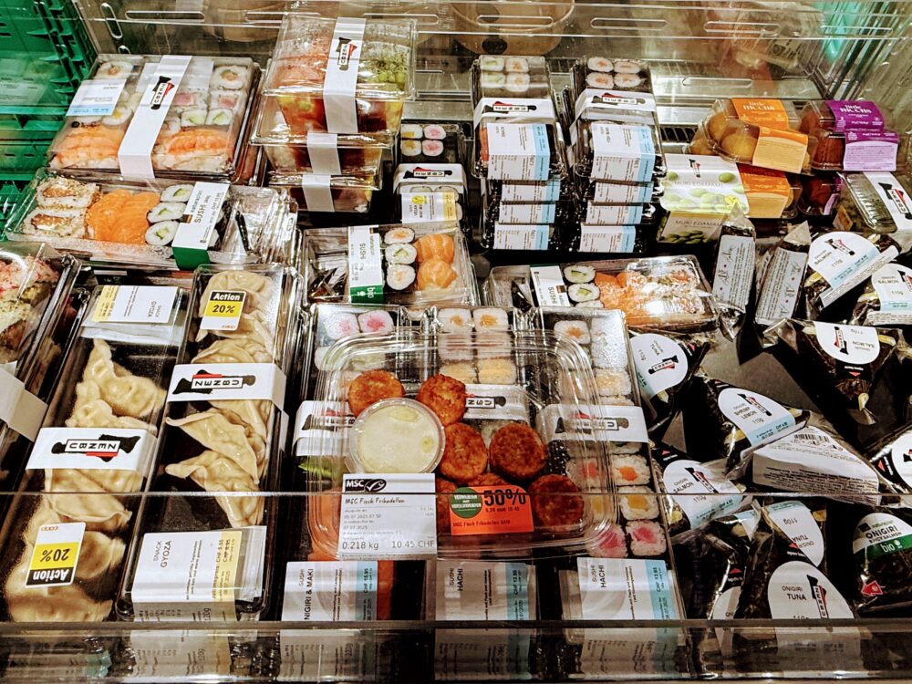 COOPの冷蔵ケースに並べられた、パック入りの寿司、おにぎり（おにぎり）、餃子（ギョウザ）、カツレツなどの惣菜。
