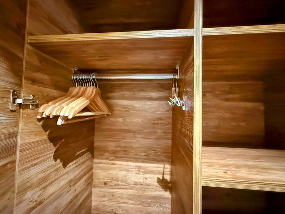 ホテルのクローゼット内部。木目調の内装で、木製のハンガーが複数かかっているハンガーラックが見える。