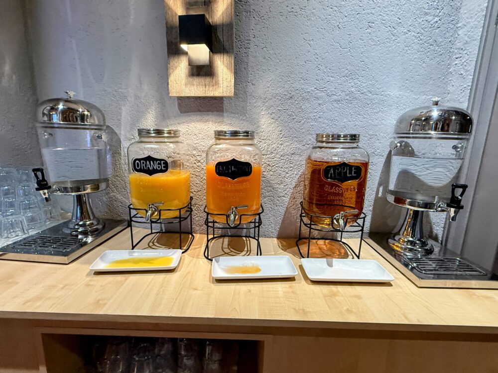 朝食ビュッフェのジュースコーナー。オレンジ、グレープフルーツ、アップルジュースの瓶が並ぶ。