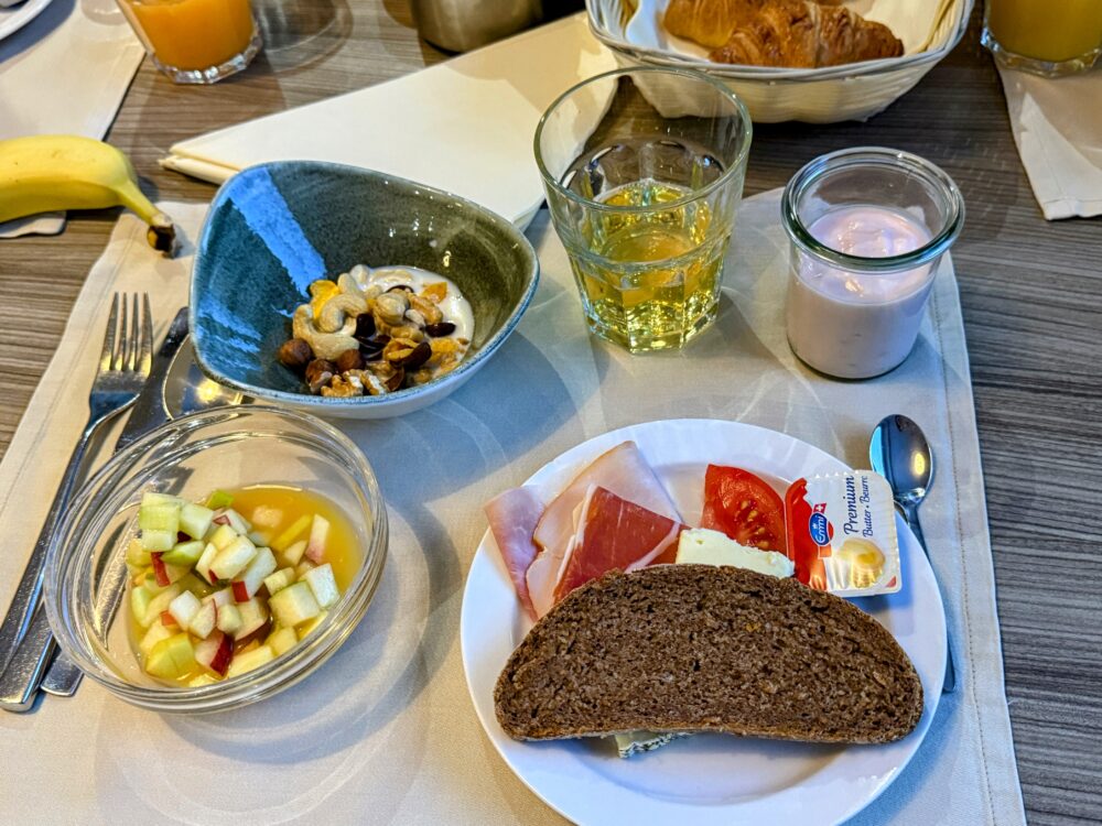 ホテル アンバサダー ツェルマットの朝食プレート。チーズ、ハム、フルーツ、パン、ヨーグルトが並ぶ。