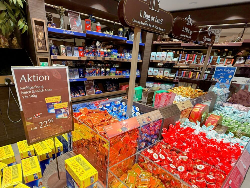 リンツチョコレートの店内の様子。量り売りのカラフルなリンドールチョコレートが山積みされ、「Aktion（セール）」の表示やスイス土産のパッケージが並んでいる。
