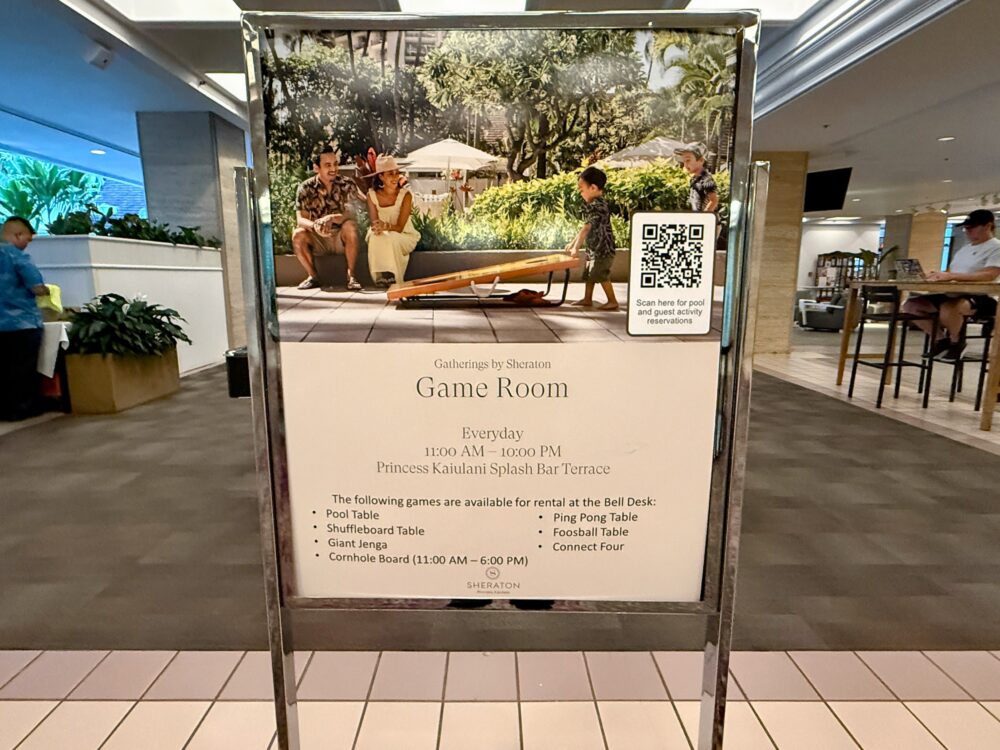 ホテル内に設けられたゲームコーナーの案内看板。屋外テラスで家族連れがジェンガなどのゲームを楽しむ様子が写っている。