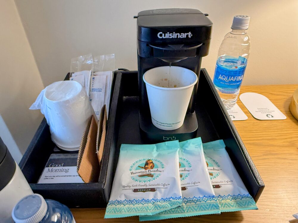 デスクに置かれたCuisinartのコーヒーメーカーとハワイアンパラダイスコーヒー、ミネラルウォーター。