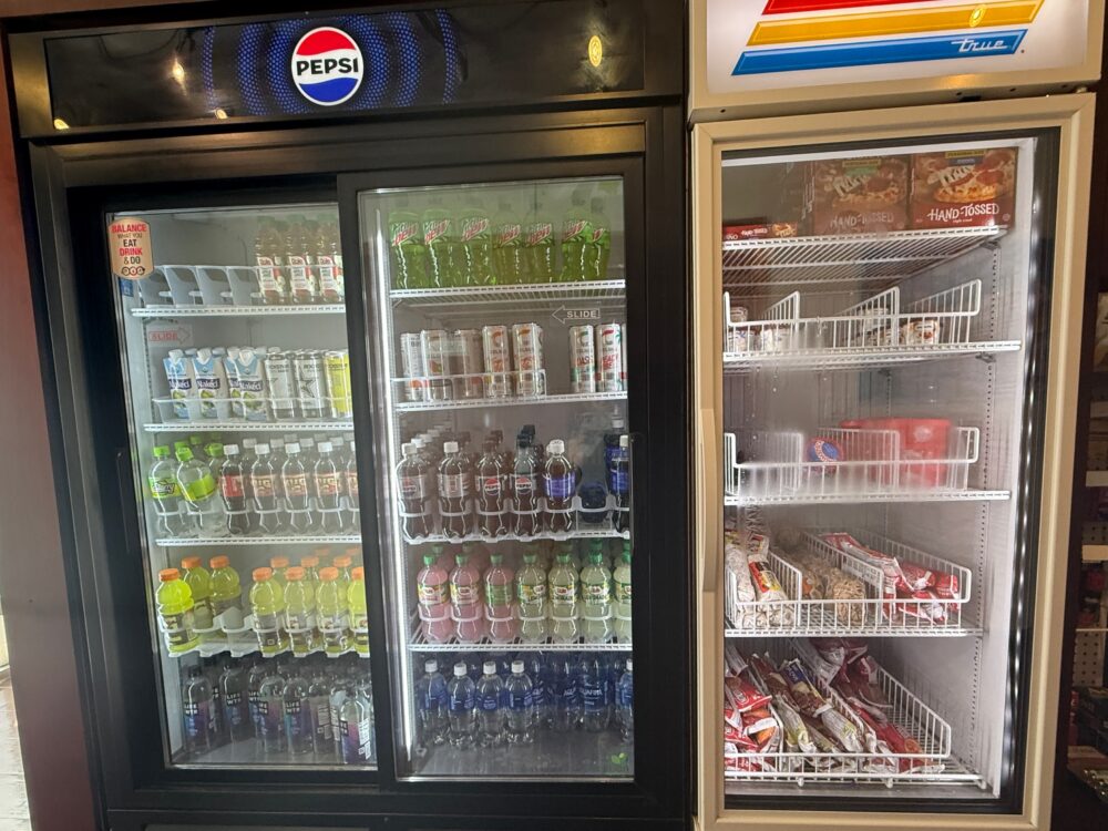 売店の飲み物（ペプシ、ジュース類）と冷凍ピザなどが陳列された冷蔵・冷凍ケース。