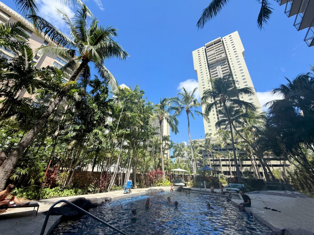 コートヤード・ワイキキ・ビーチの屋外温水プール。ヤシの木に囲まれたプールと周囲の高層ビル。