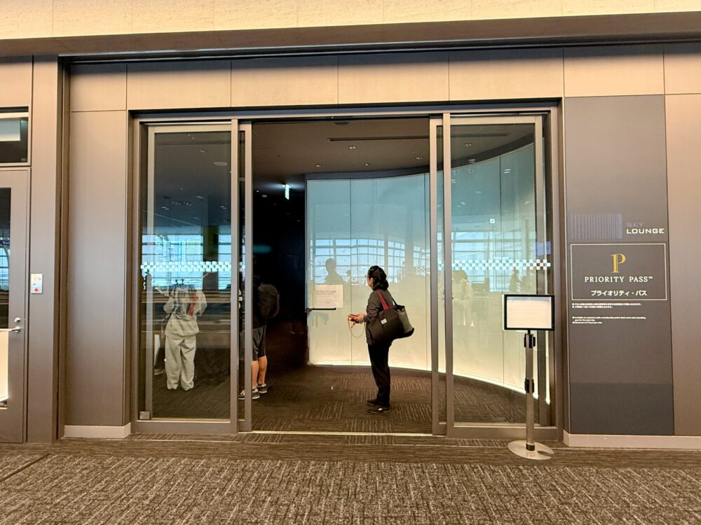 羽田空港第3ターミナルのSky Lounge South入口。プライオリティパスの看板があり、数名が受付で手続きをしている様子。