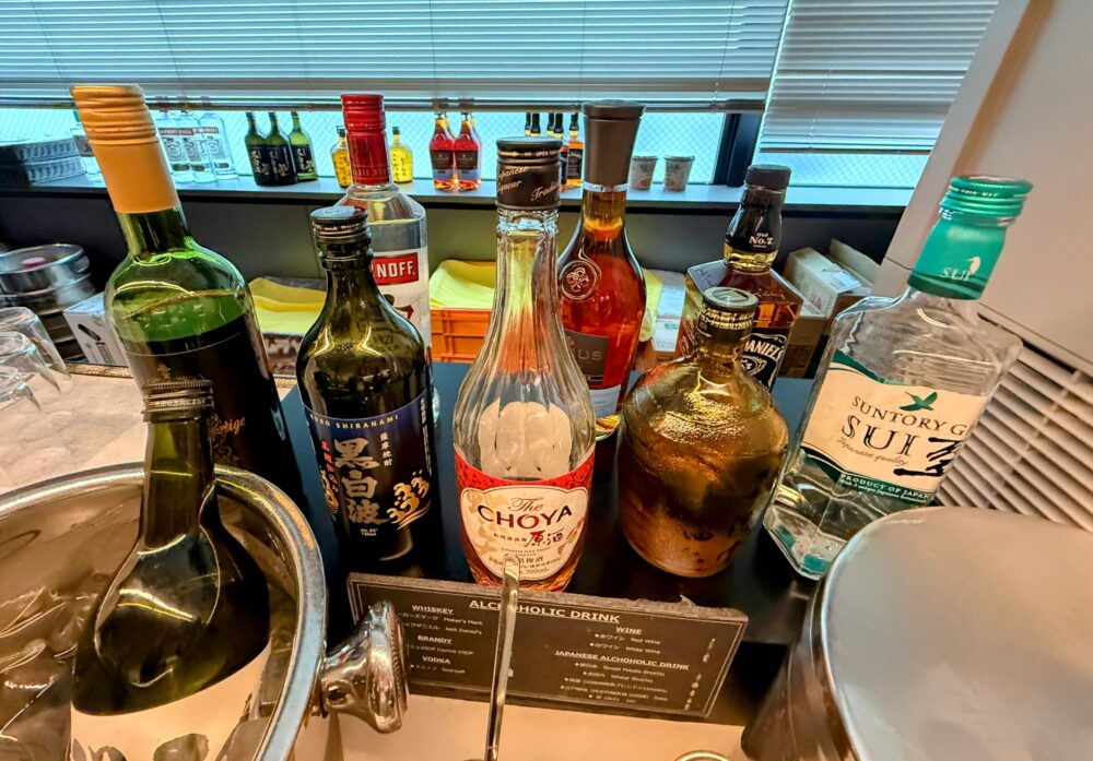 ウイスキーや焼酎、梅酒などのアルコール類が並ぶ棚。サントリーSUI、チョーヤ梅酒、ジャックダニエルなどのボトルが見える。