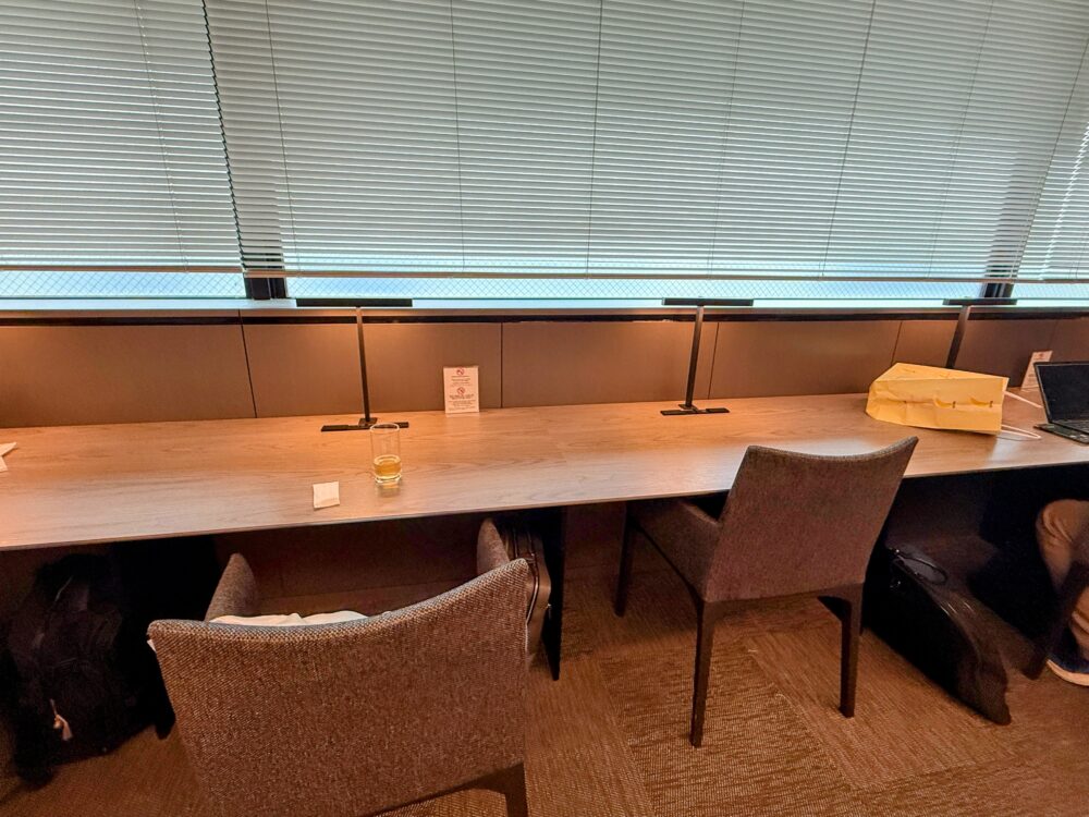 窓際のカウンター席。ブラインド越しに滑走路の光が入り、落ち着いた雰囲気でパソコン作業をする利用者の姿。