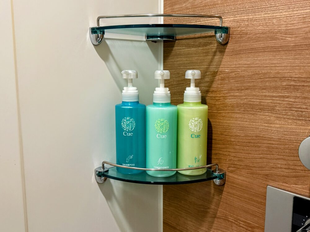 シャンプー、コンディショナー、ボディソープが棚に並んでいる。ブランドはCue。