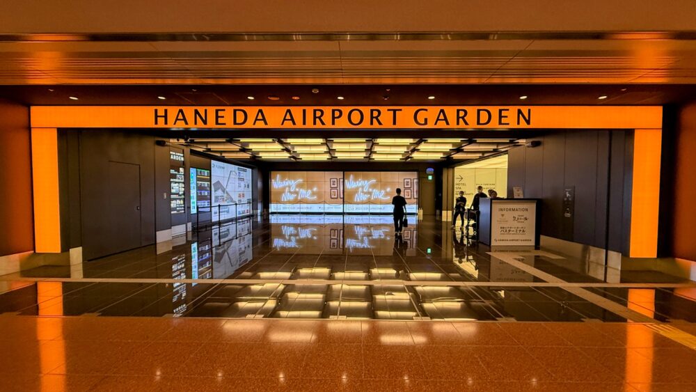 羽田エアポートガーデンのエントランス。床が磨かれて光っており、大きな「HANEDA AIRPORT GARDEN」の文字とデジタルサイネージが見える。