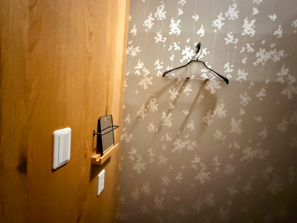 施術室の壁の設備。着替え用のハンガー、コンセント、スマートフォンなどを置ける便利な棚が設置されている。