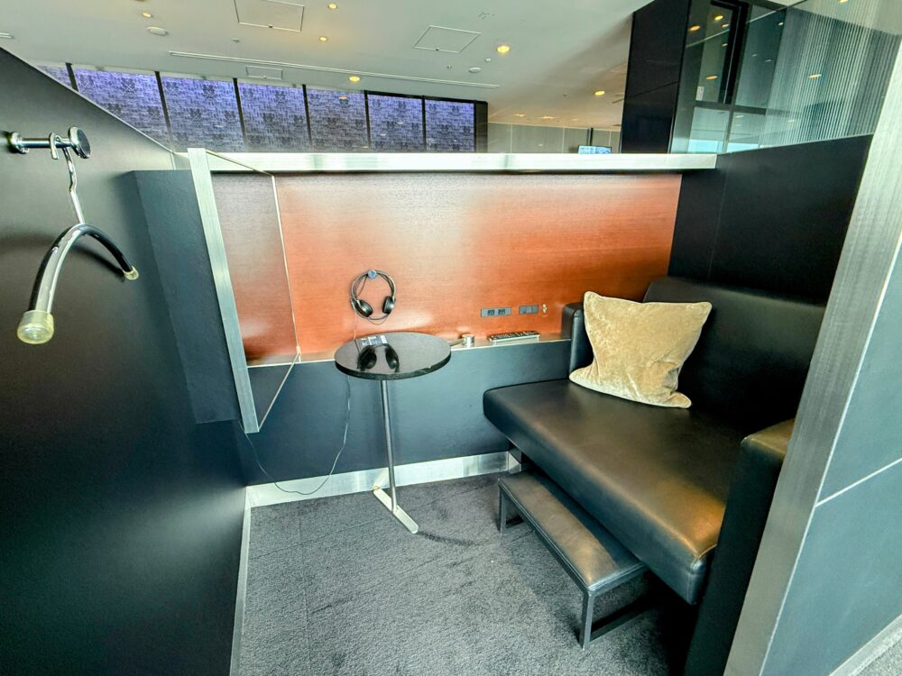 ANAスイートラウンジにある、ヘッドホンと小さなサイドテーブル、コートハンガーが設置されたプライベート感のある半個室ブース席。