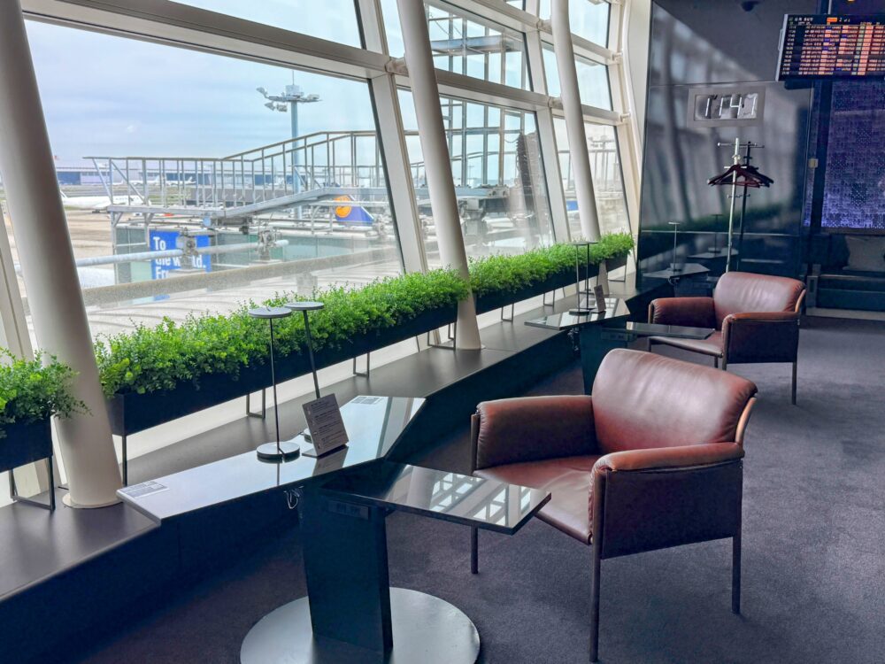 植栽が置かれた窓際に配置された、濃い茶色の革張りチェア。滑走路と駐機中の航空機が見える、羽田ANAスイートラウンジの窓際席。