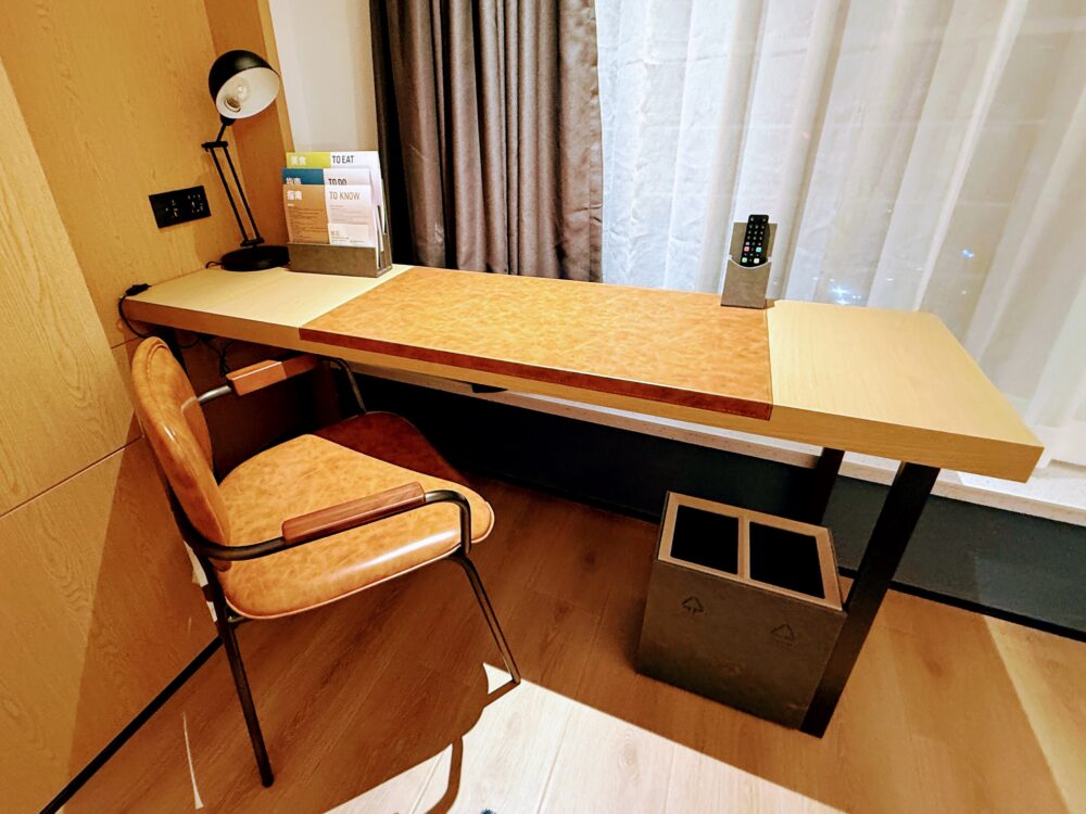 客室内のワークデスク。木目調のシンプルなデザインで、椅子とスタンドライト、各種案内が置かれている。作業スペースとしても十分な広さ。