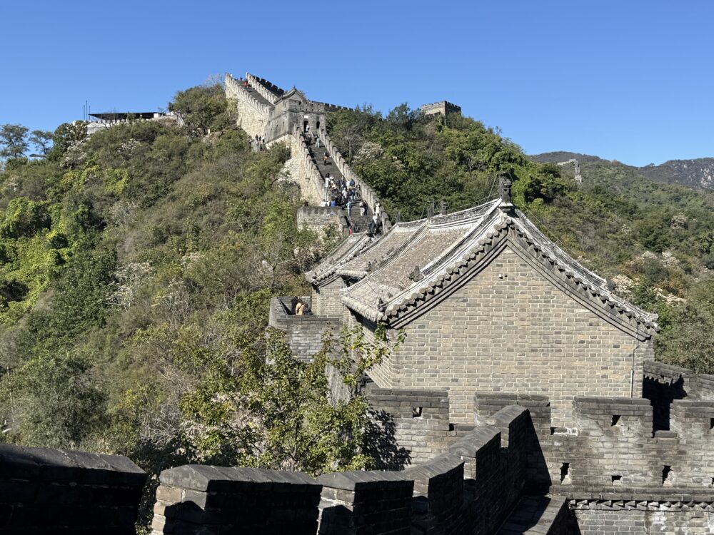 慕田峪長城の4号故楼「正関台」の外観。石造りの建物が山の斜面に建ち、青空の下で美しいカーブを描く城壁が続く。