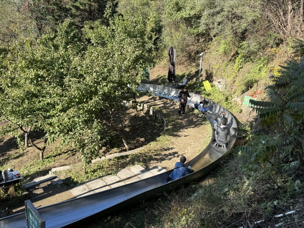 慕田峪長城のトボガン滑走コース。曲がりくねったレールを座席付きスライダーで滑る観光客たちの様子。