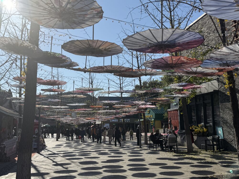 慕田峪長城ふもとの商業エリアに並ぶ傘のアート装飾。通りの上にカラフルな傘が吊るされ、観光客が歩いている。