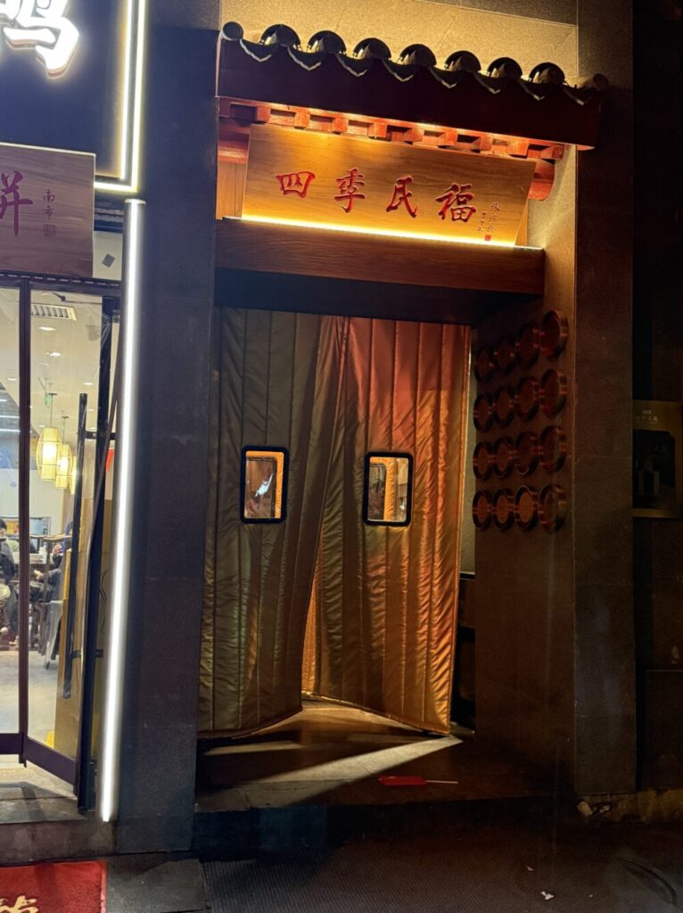 北京・四季民福烤鴨店 南池子大街店の入口。木製の看板と金色の防寒カーテンがライトに照らされている夜景。