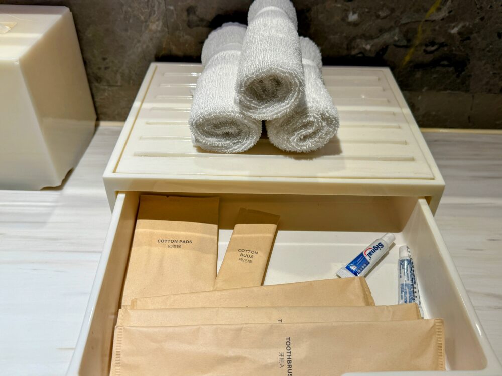 洗面台横のアメニティセット。歯ブラシやコットン、綿棒、タオルなど基本的なアイテムが揃っている。