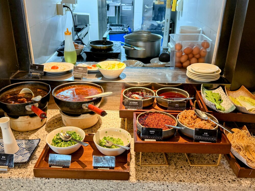 朝食ビュッフェのライブキッチンコーナー。卵料理とヌードル料理の調理カウンターが並び、各種スープや具材が並んでいる様子。
