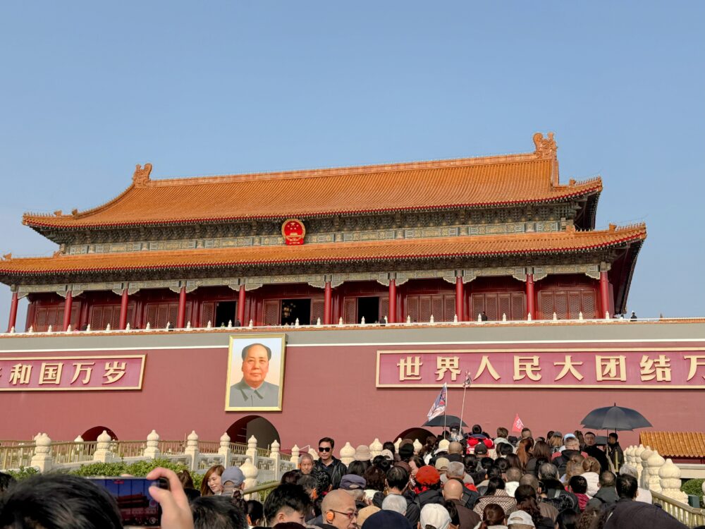 天安門前に集まる大勢の観光客と、建物中央に掲げられた毛沢東の肖像画。赤い城壁と金色の装飾が際立つ天安門の近景。