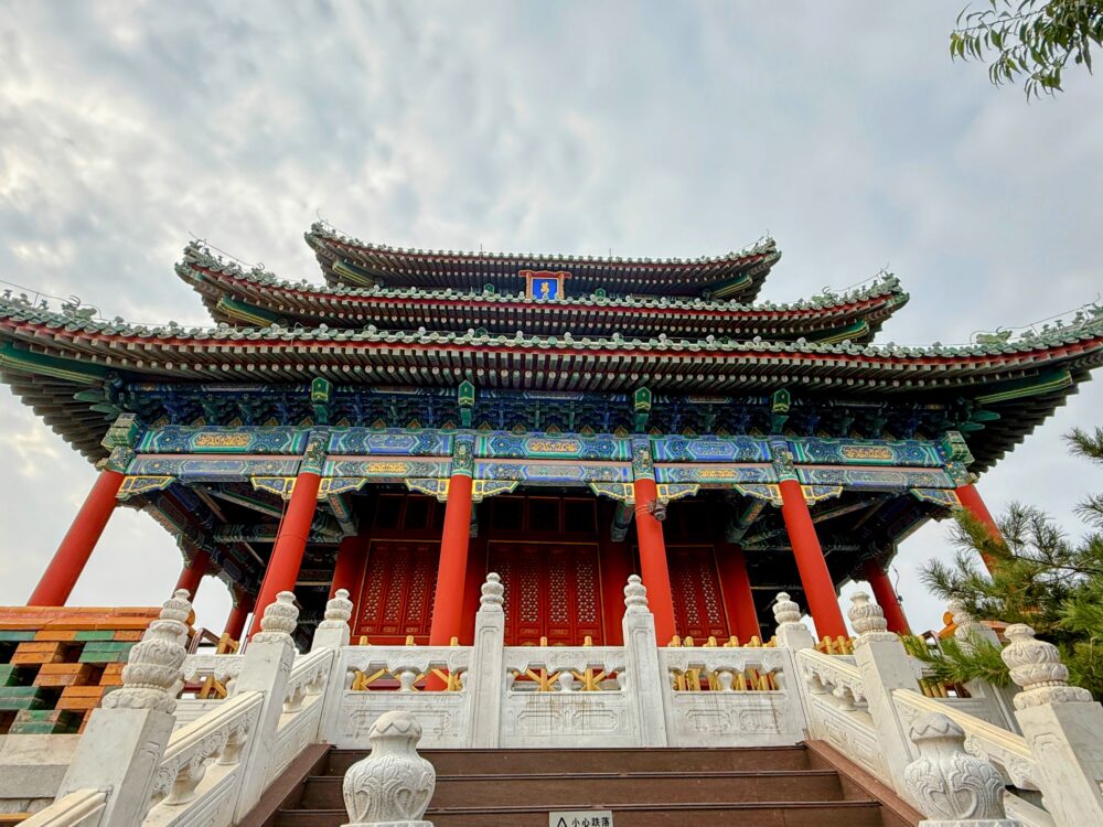 景山公園山頂にある万春亭を下から見上げて撮影した写真。朱色の柱と緑と青の装飾が施された多層屋根が特徴的。