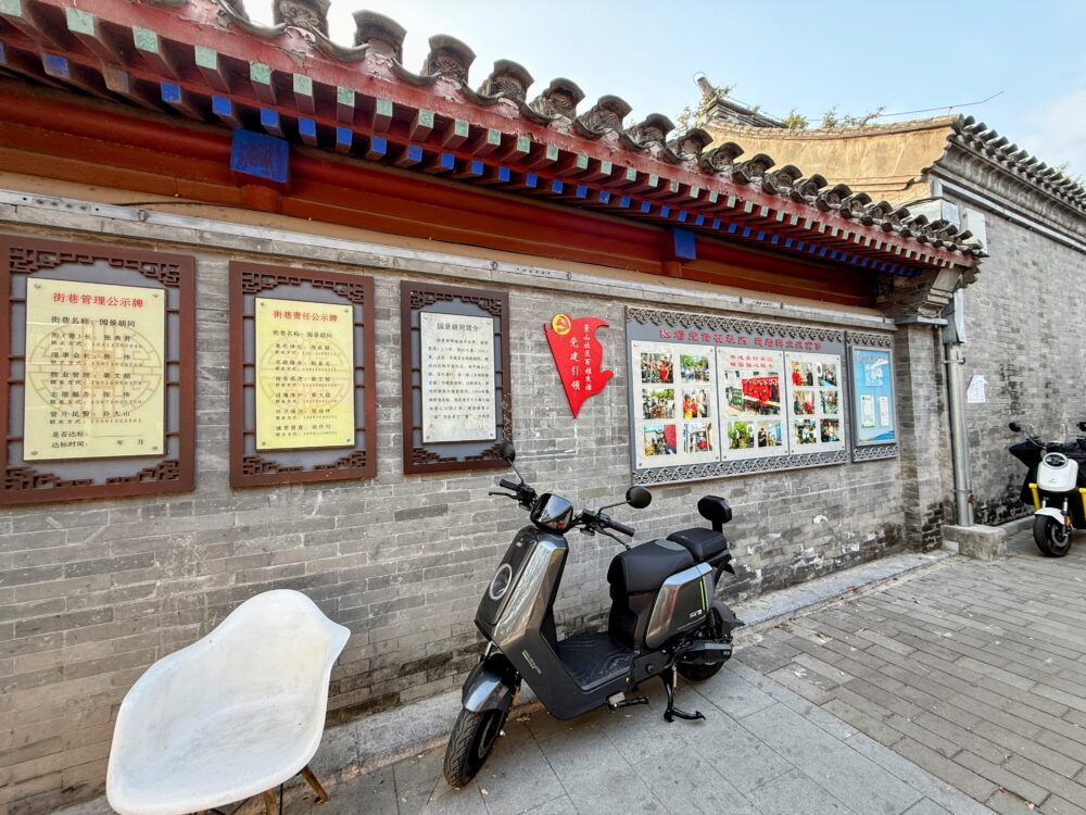 胡同の壁に掲示された住民向けのお知らせ掲示や写真パネル、電動バイクが置かれた様子