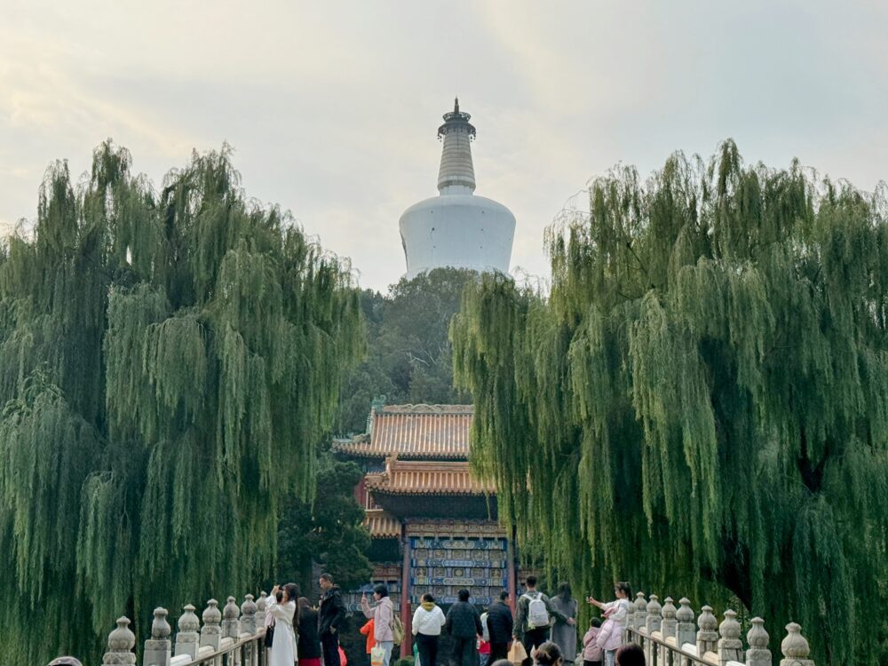 湖にかかる橋の先に白い仏塔「白塔」がそびえ、両側に大きな柳の木が垂れ下がる北海公園の象徴的な風景。