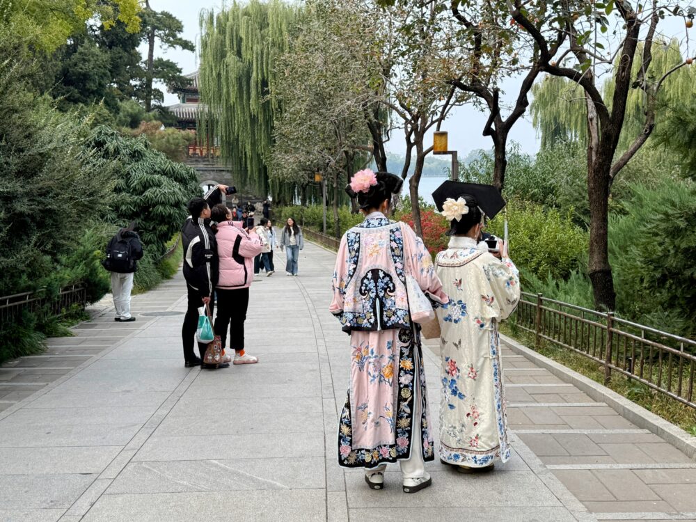 漢服姿の女性たちが並木道を歩き、観光客が写真を撮っている北海公園の散策路。