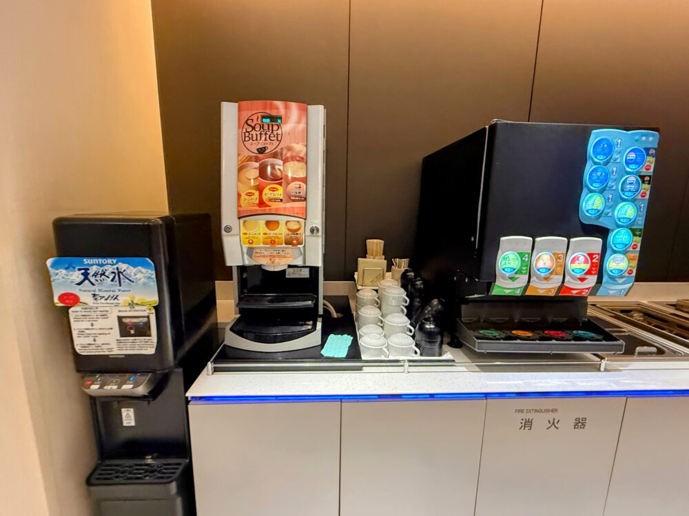 羽田空港ANAスイートラウンジのドリンクコーナー。スープバーやソフトドリンクマシン、サントリー天然水サーバーが並び、スープやジュース、コーヒーなどを自由に楽しめる。