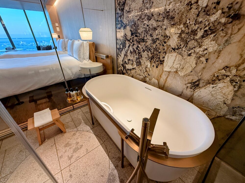 ガラス越しにベッドルームと外の景色が見える、大きく深めの白いバスタブ