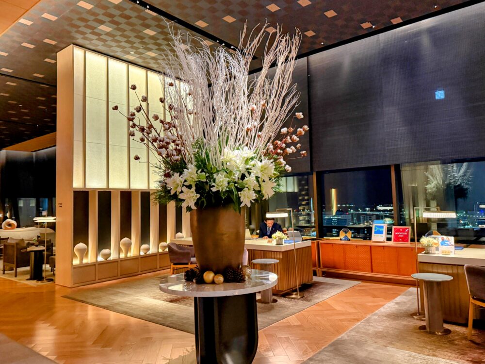 リッツ・カールトン福岡18階ロビー。ダイナミックな白い枝と花の生け花と、奥に広がる福岡の夜景