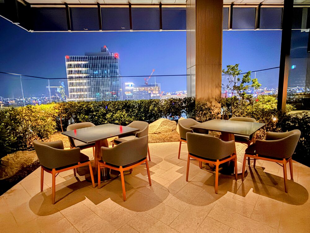 18階にある屋外テラス席。テーブルセットとガラス手すりの向こうに見える福岡のビルの夜景。
