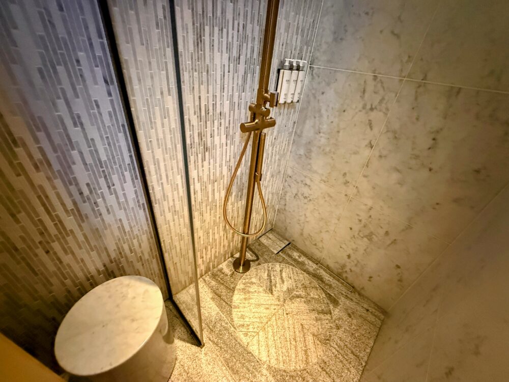 大理石の壁とゴールドのシャワーヘッドが特徴的な個室シャワーブース