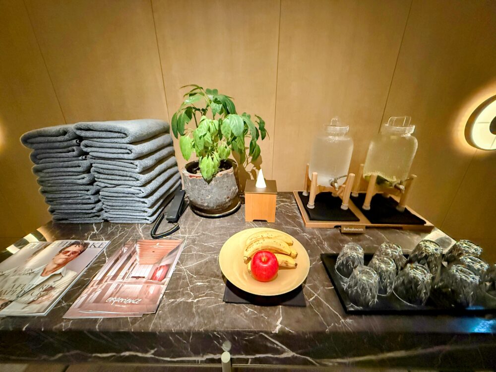 プールサイドに用意されたリフレッシュメント。タオル、デトックスウォーター、バナナ、リンゴが置かれている