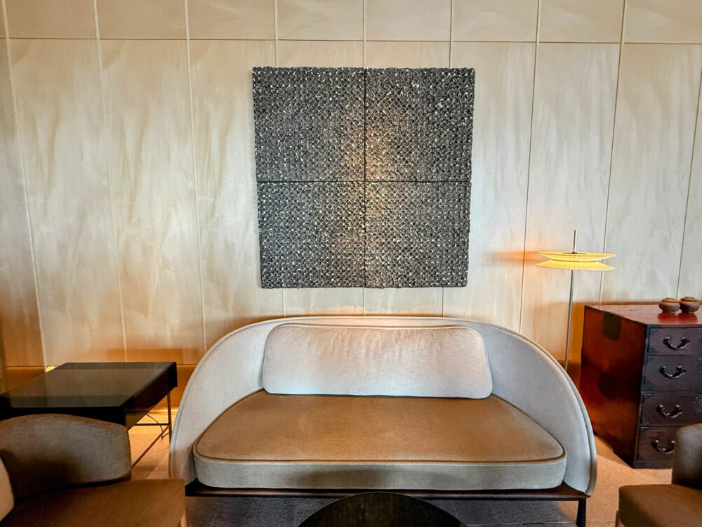 ソファーの後ろの壁に飾られた、正方形の立体的なアート作品と間接照明