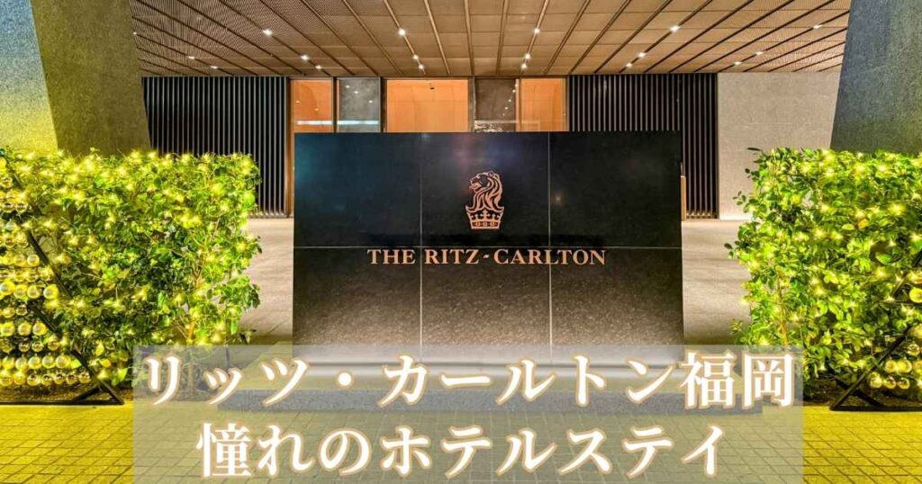 夜にライトアップされたリッツ・カールトン福岡のエントランス。黒い大理石のサインに「THE RITZ-CARLTON」のロゴが輝き、周囲には温かみのあるイルミネーションが飾られている。