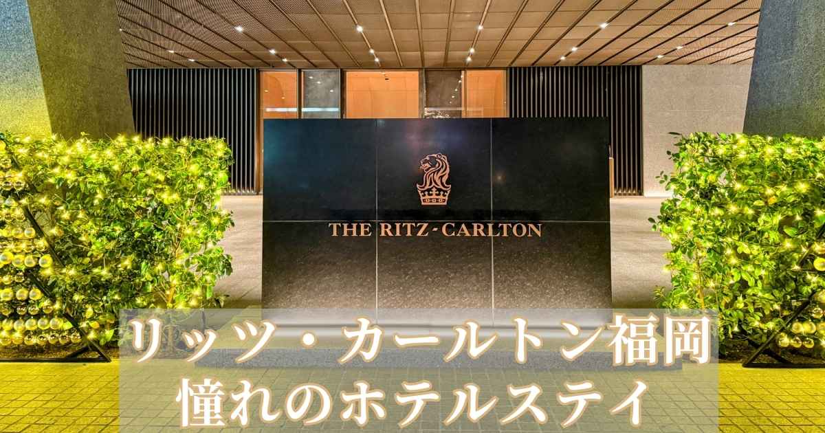 夜にライトアップされたリッツ・カールトン福岡のエントランス。黒い大理石のサインに「THE RITZ-CARLTON」のロゴが輝き、周囲には温かみのあるイルミネーションが飾られている。