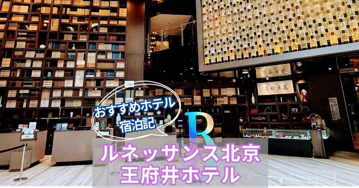 ルネッサンス北京王府井ホテルのロビー全景。天井まで届く本棚デザインの壁と、金色に輝くアート照明が印象的。中央にはカラフルな「R」ロゴが配置され、高級感あふれる雰囲気を演出している。