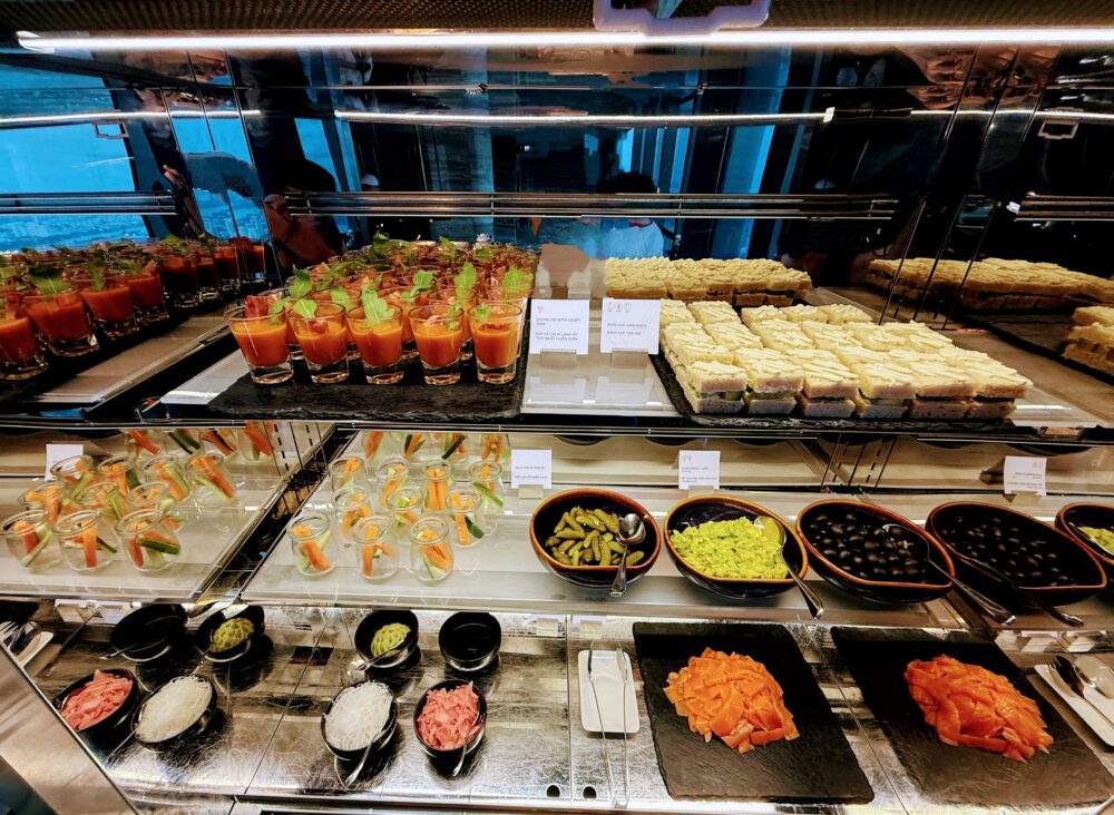 ガラスケースに陳列された色とりどりの冷菜。スモークサーモン、アボカドサンドイッチ、ピクルス、オリーブ、ガスパチョなどが並ぶ。