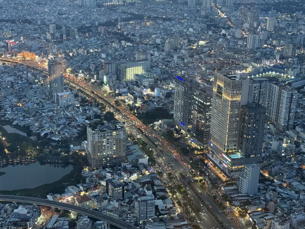 ヴィンパール ランドマーク81の高層階から見下ろすホーチミン市内の夕暮れの景色。車のライトが連なる大通りと、立ち並ぶ高層ビル群が青い夕闇に浮かび上がっている。