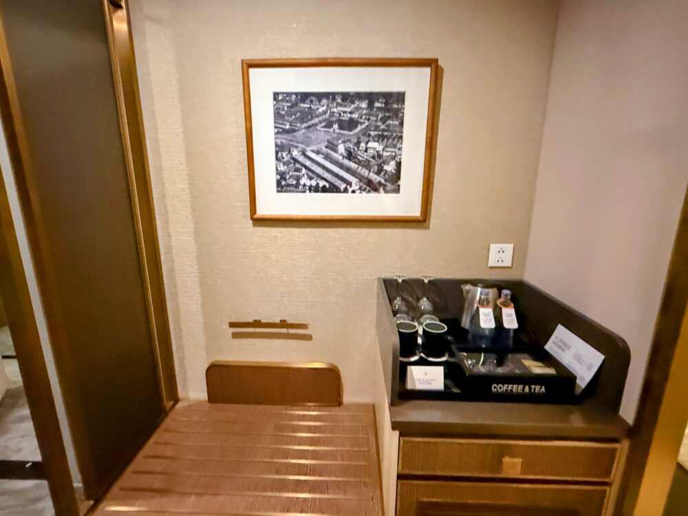 客室入口付近にあるミニバーコーナー。壁にはモノクロ写真が飾られ、棚の上にはドリンクセット、左側には荷物置き場がある。
