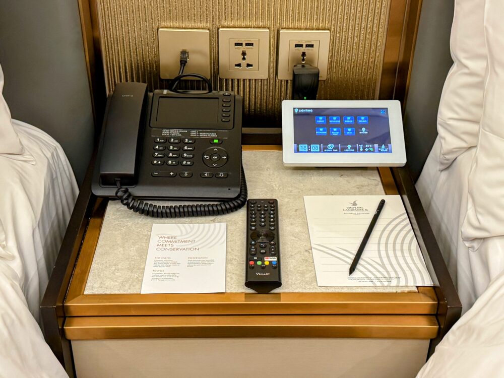 ベッドサイドテーブルにある電話、部屋の照明操作用タブレット、テレビリモコン。壁には日本のプラグも使えるユニバーサルコンセントとUSBポートがある。