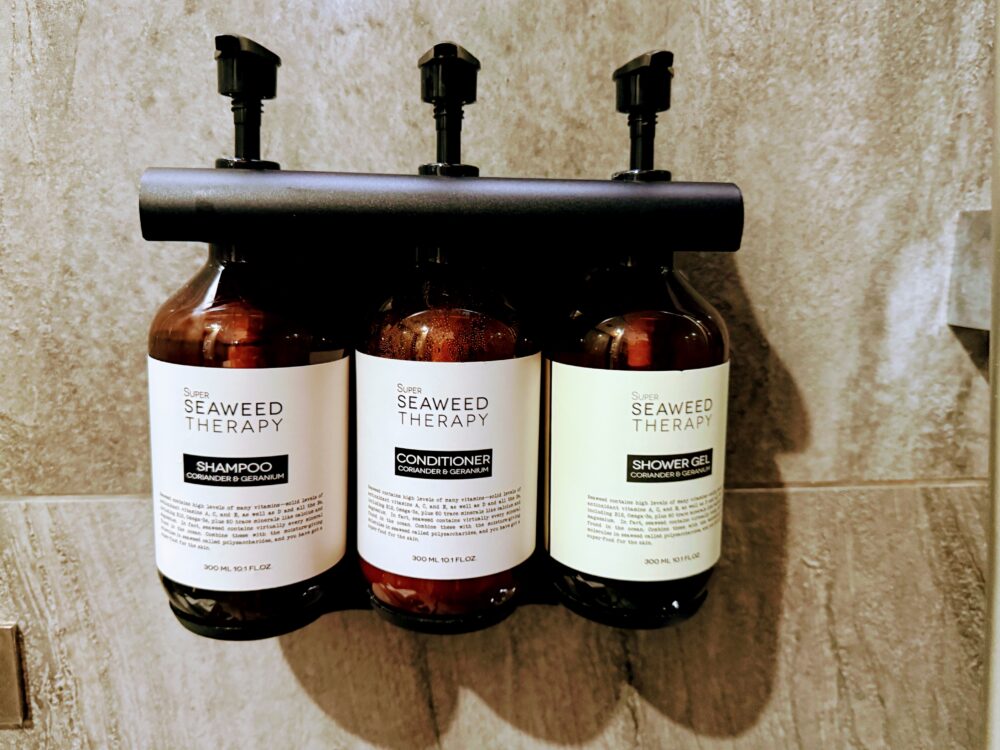 シャワーブース内に設置された「Super Seaweed Therapy」ブランドのシャンプー、コンディショナー、シャワージェルのボトル。